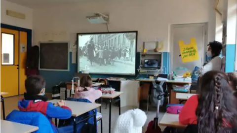 Bambini di spalle seduti in aula mentre guardano un film in bianco e nero